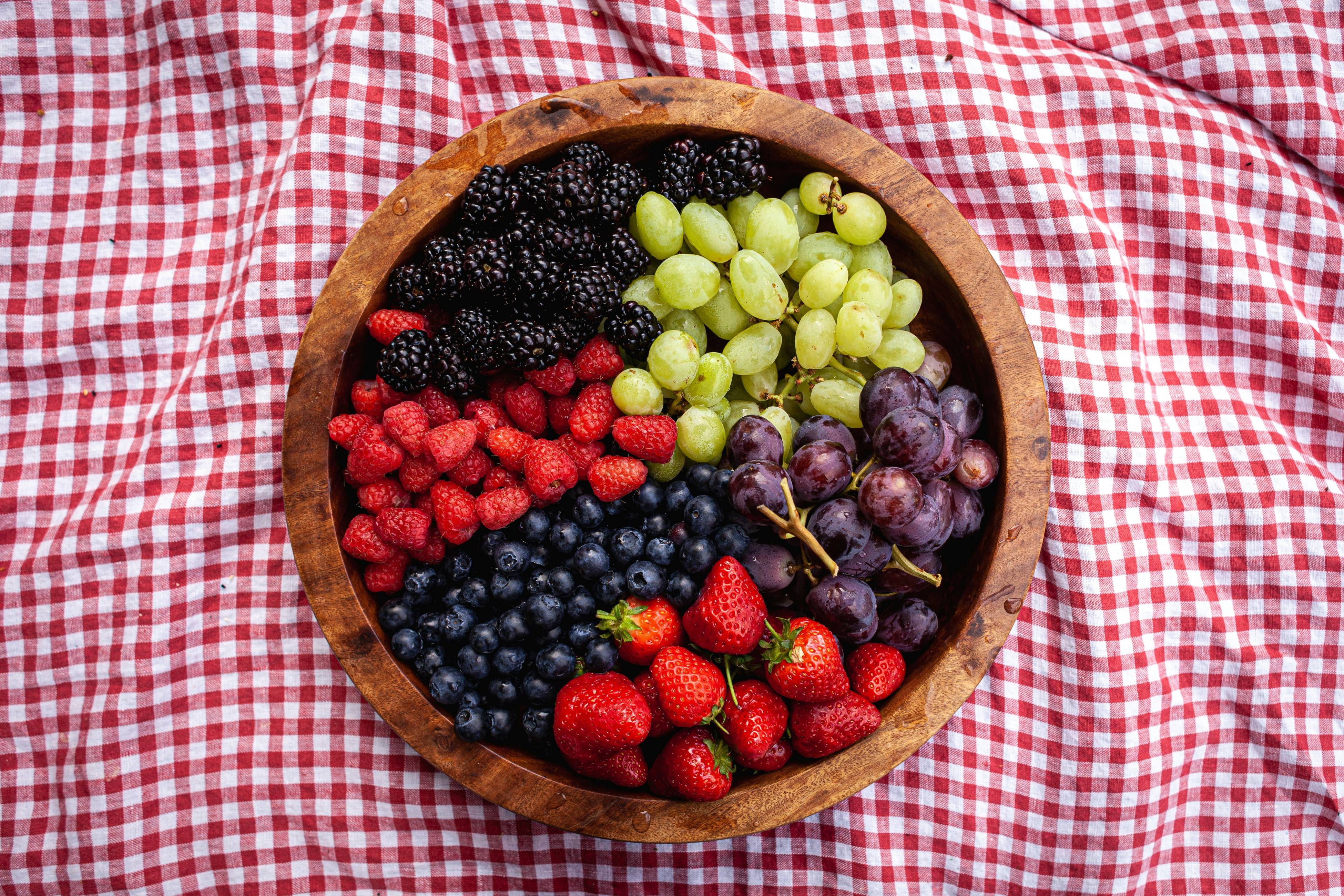 a wooden bowl filled with berries and grapes