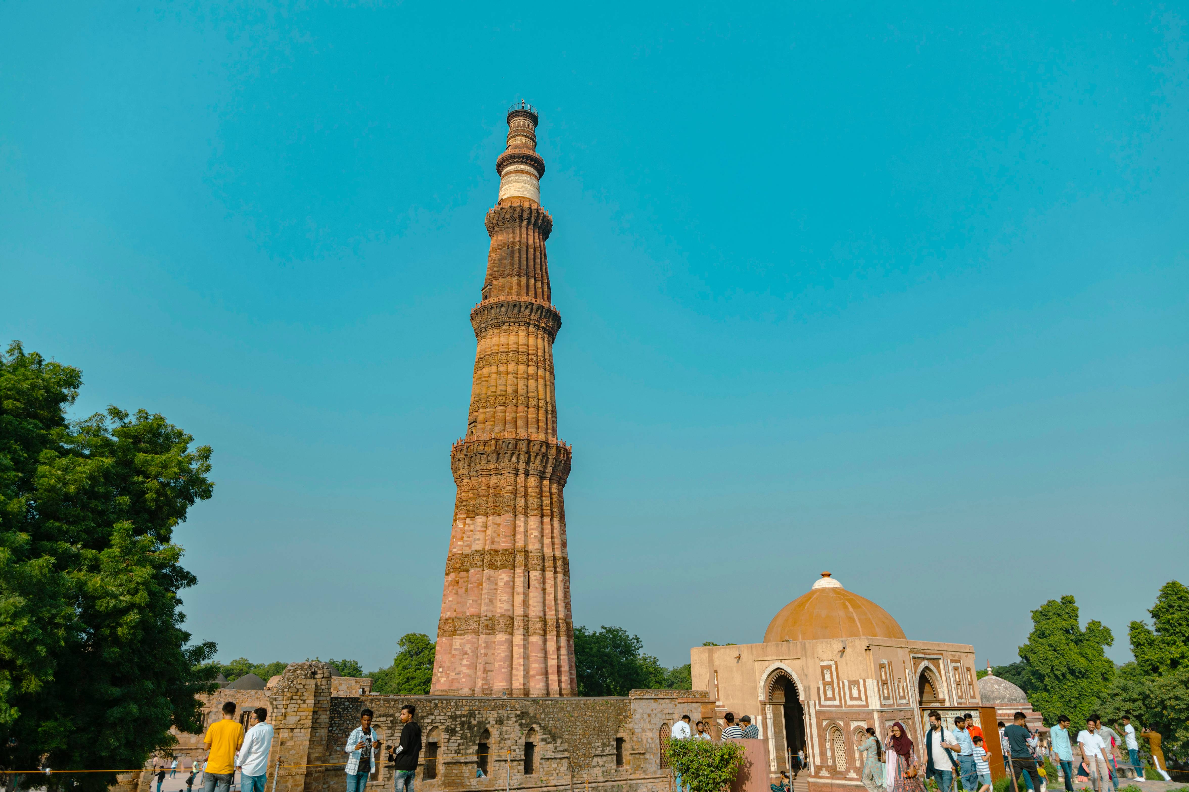 a tall tower with people around it with Qutub Minar in the background